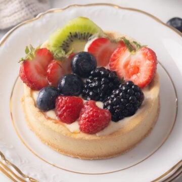 A gluten free fruit tart topped with sliced kiwi, strawberries, blueberries, blackberries, and raspberries on a white plate with a gold rim.