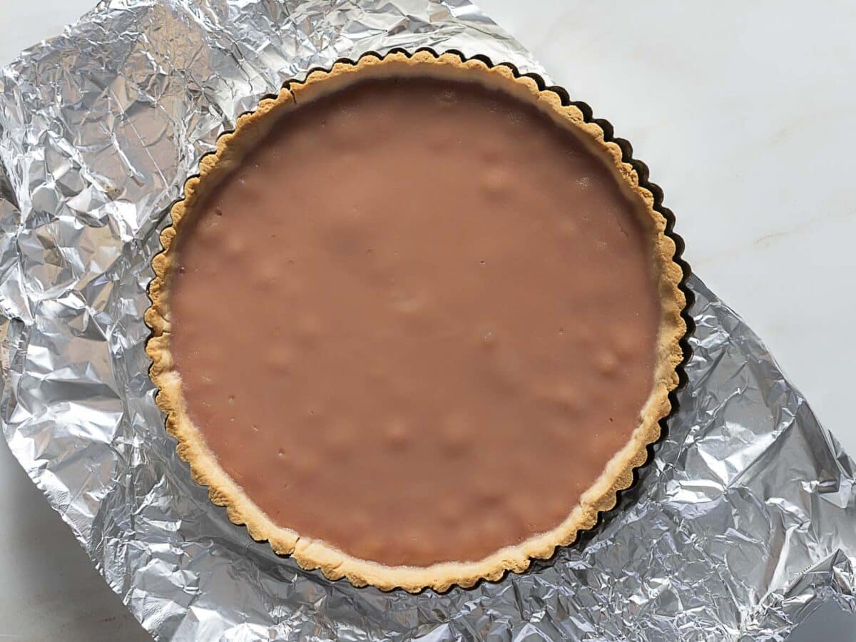 A chocolate tart with a smooth filling in a pastry crust, placed on a sheet of crumpled aluminum foil.
