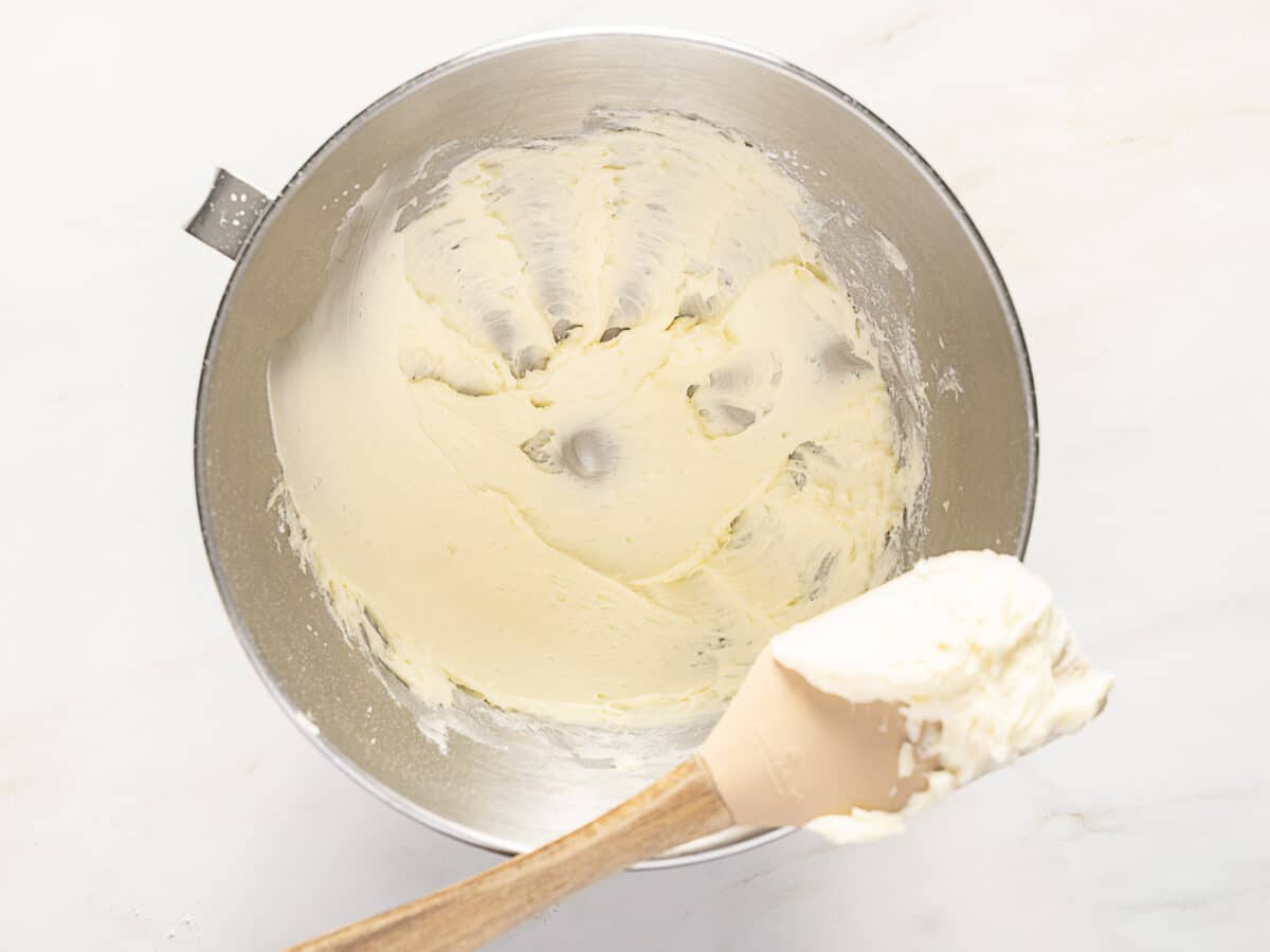 A metal mixing bowl with whipped cream or frosting and a spatula resting on the side, ready for filling a sweet tart dough or gluten free pâte sucrée creation.