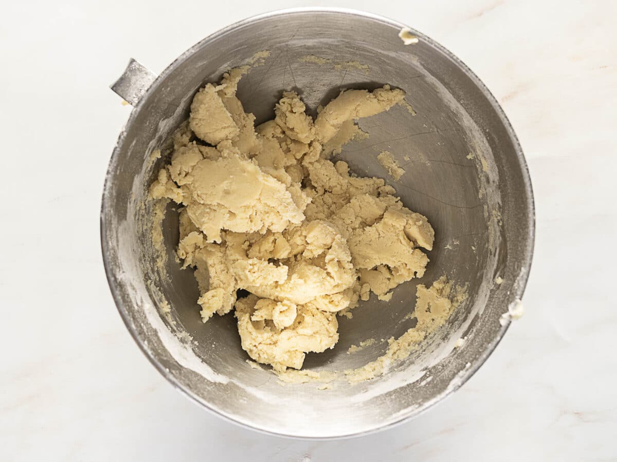 A stainless steel mixing bowl contains a partially mixed, pale Gluten Free Sweet Tart Dough on a light-colored surface.