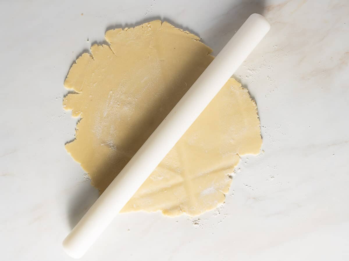 A white rolling pin rests on rolled-out Sweet Tart Dough on a lightly floured marble surface.