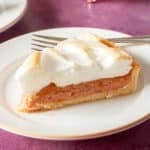A slice of pie with a golden crust, a fruit filling, and a layer of fluffy meringue on top, served on a white plate with a fork.