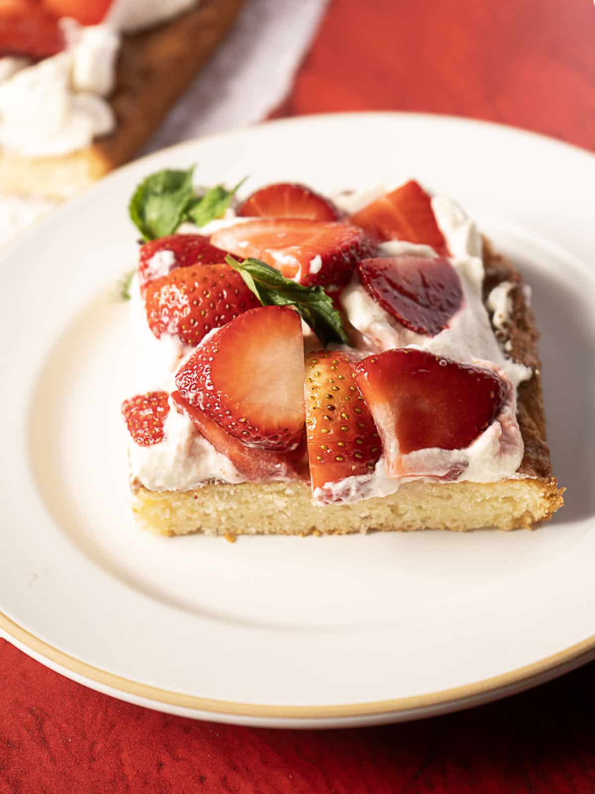 A slice of cake topped with whipped cream and fresh sliced strawberries sits on a white plate.