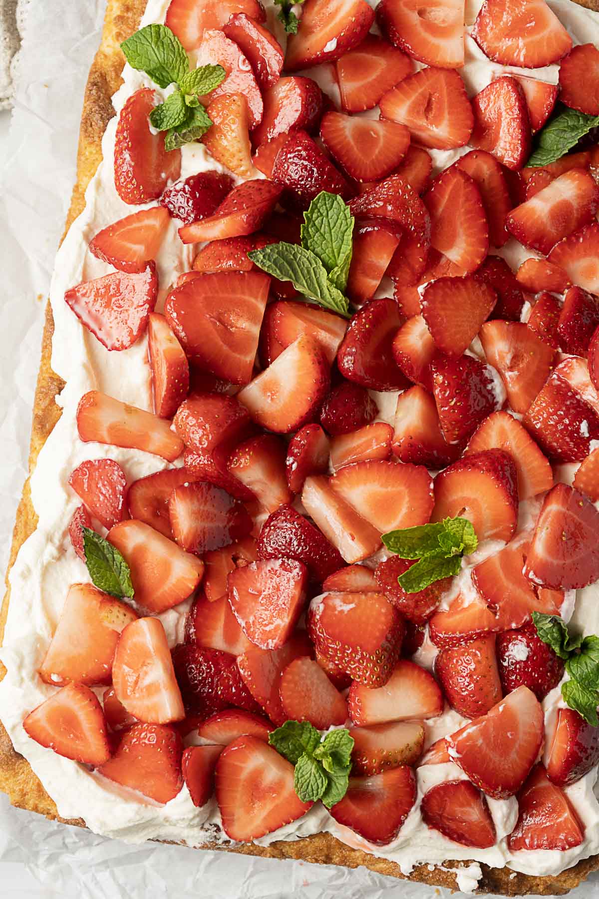 A close-up of a dessert topped with whipped cream, sliced strawberries, and mint leaves on a pastry crust.