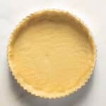 A round tart pan filled with unbaked gluten free tart shell on a marble surface.