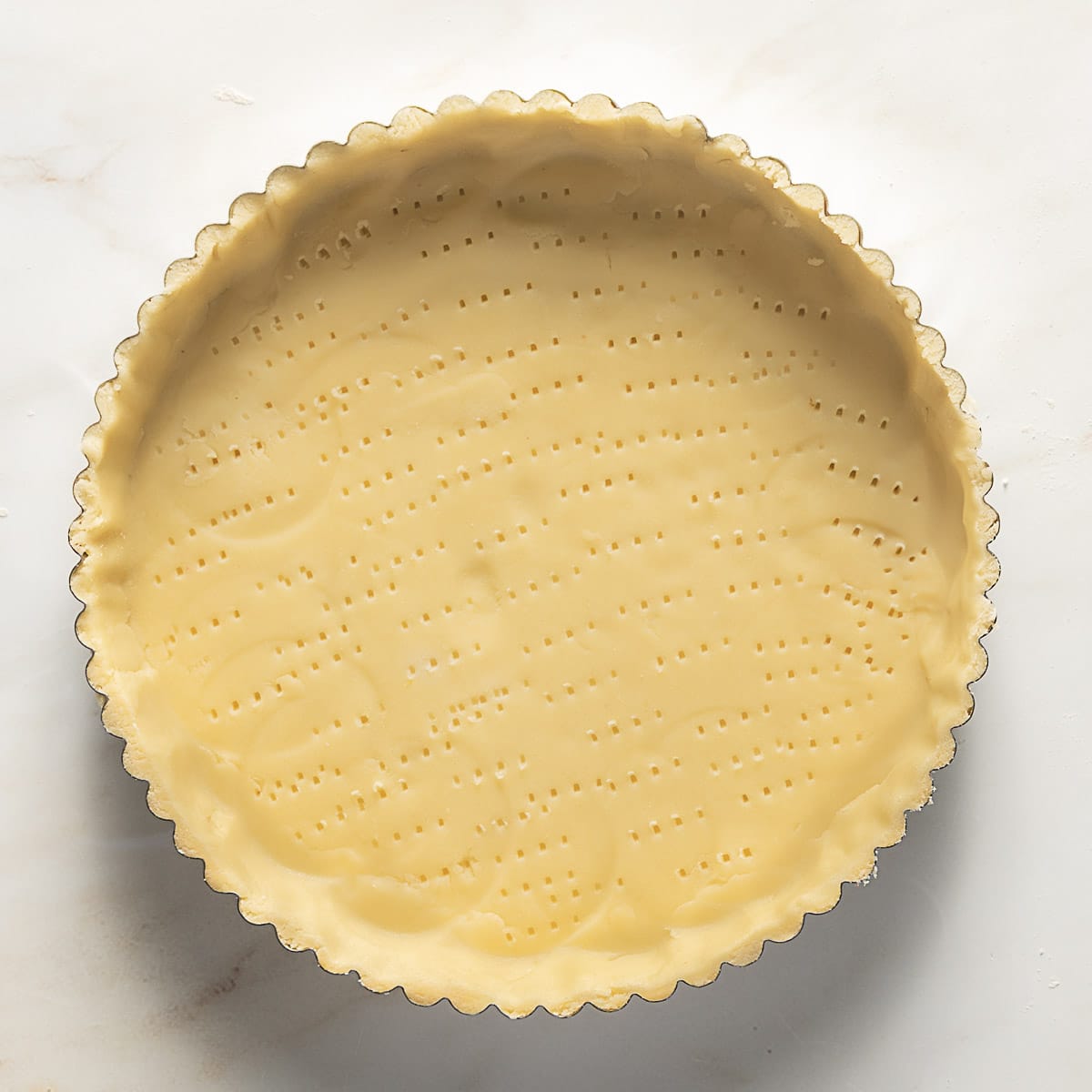 A round tart pan filled with unbaked gluten free tart shell on a marble surface.