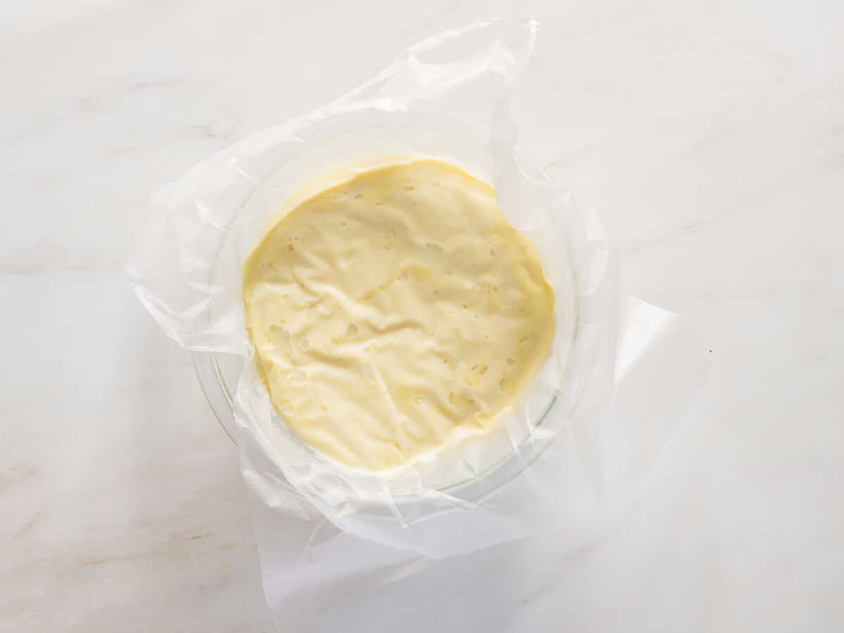 A bowl lined with parchment paper filled with a thick, pale yellow batter, resting on a light-colored marble surface.