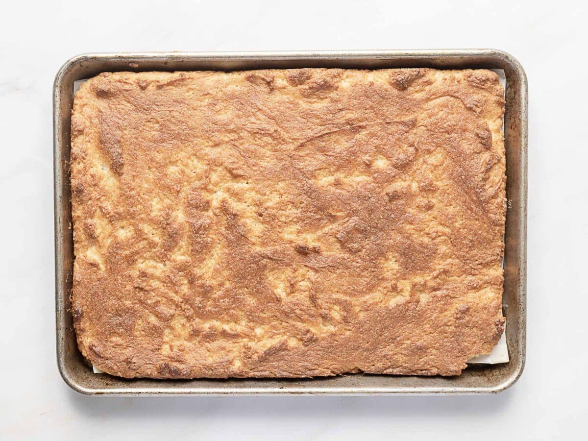 A rectangular baking sheet filled with a large, evenly baked golden-brown crust or bar on a white surface.