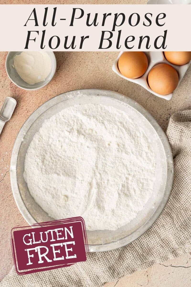A plate of gluten free flour blend labeled "gluten free" sits on a cloth, with eggs and a measuring spoon nearby on a beige surface.