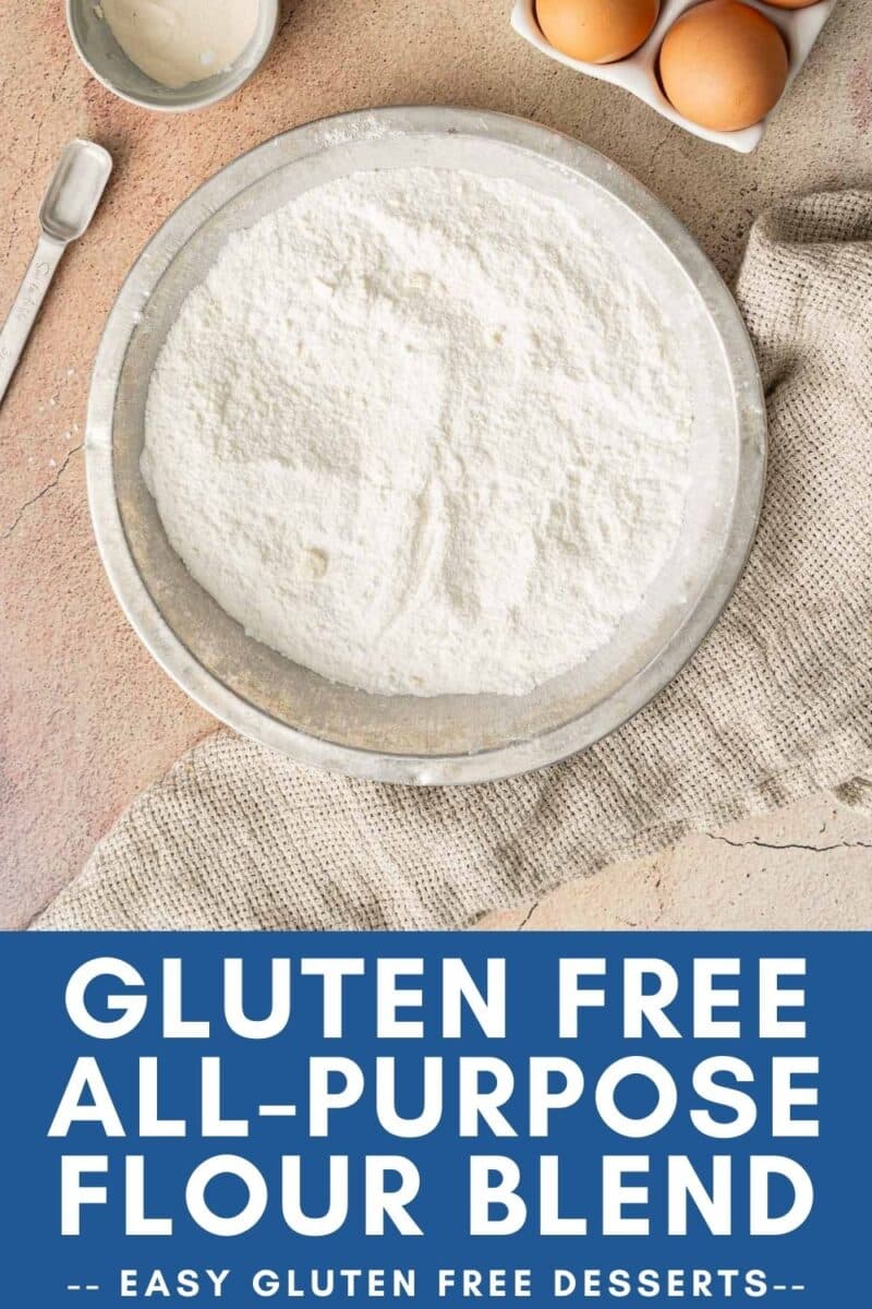 A bowl of gluten free flour blend sits on the countertop, surrounded by eggs, a small bowl, and a measuring spoon.