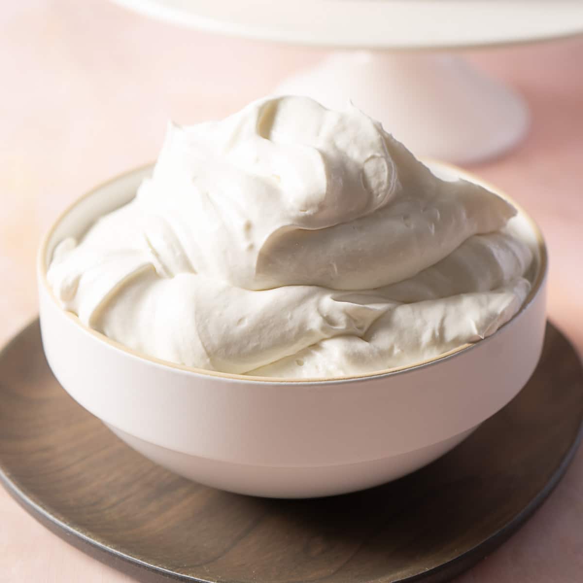 A white bowl filled with thick, creamy whipped frosting sits on a wooden plate.
