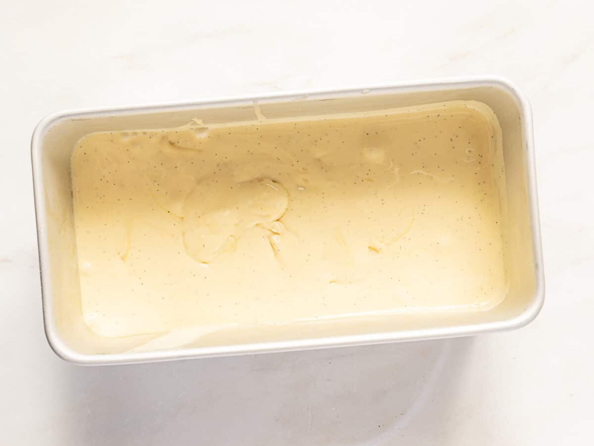 Rectangular metal loaf pan filled with smooth, pale yellow cake batter, set on a light-colored surface.