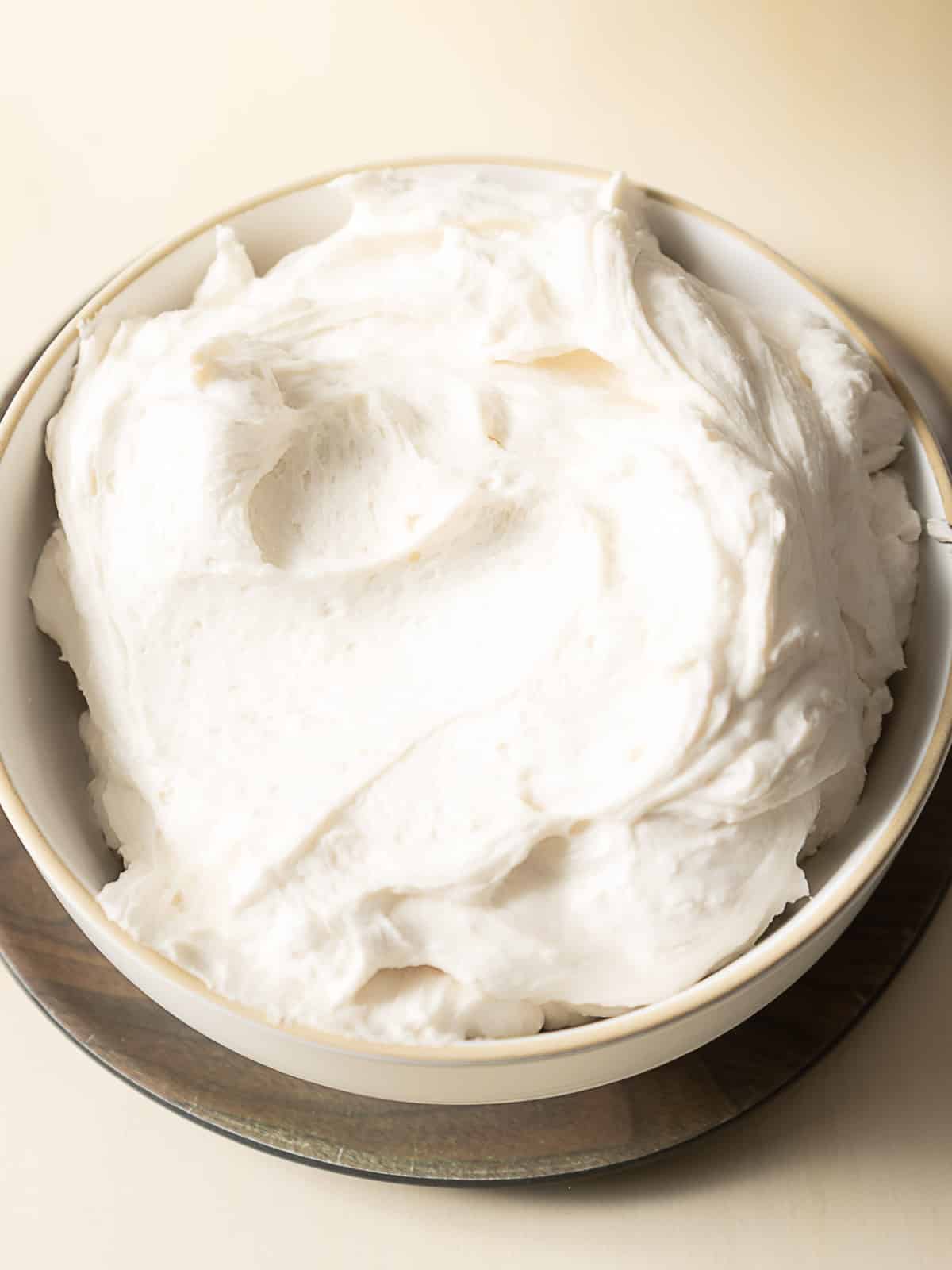 A white bowl filled with a large amount of fluffy white whipped frosting sits on a wooden surface.