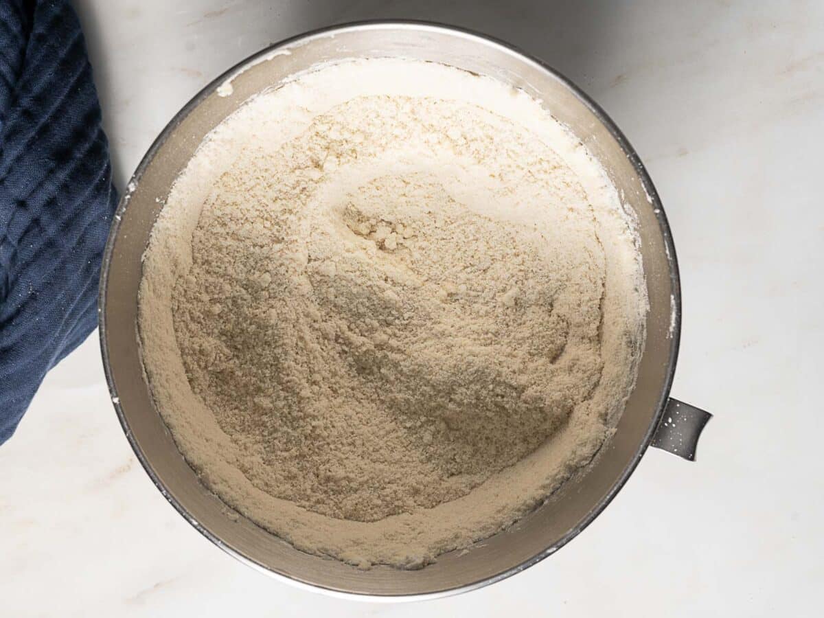A metal mixing bowl filled with dry flour mixture sits on a light-colored countertop.