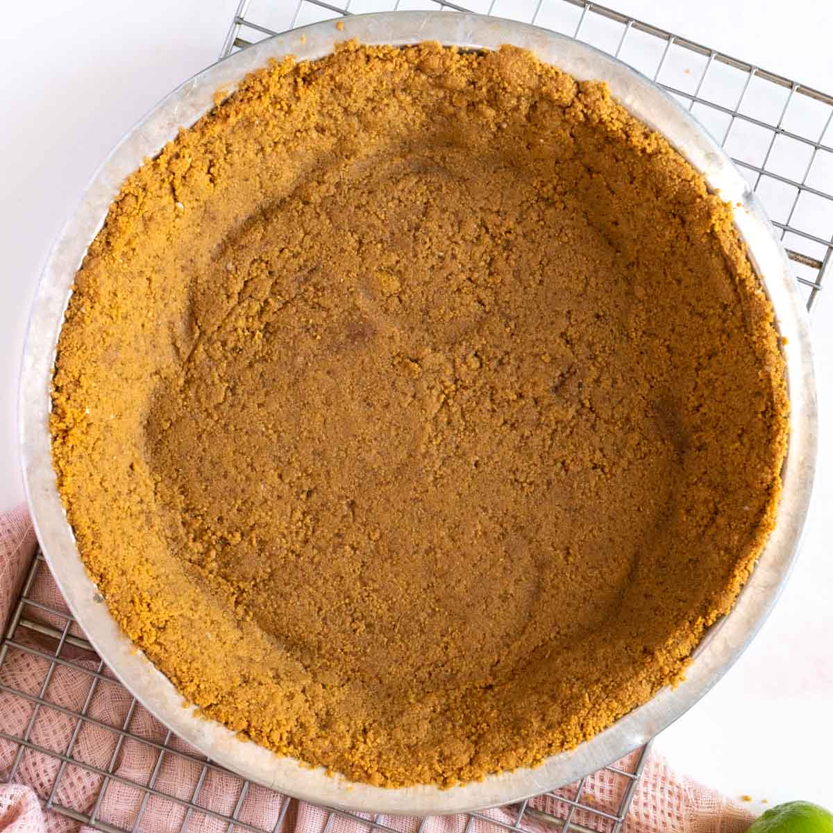 A metal pie dish filled with an even layer of crumbly graham cracker crust, resting on a cooling rack.