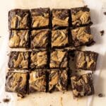 Top-down view of sixteen chocolate brownies with a swirled peanut butter topping, arranged in a grid on parchment paper.