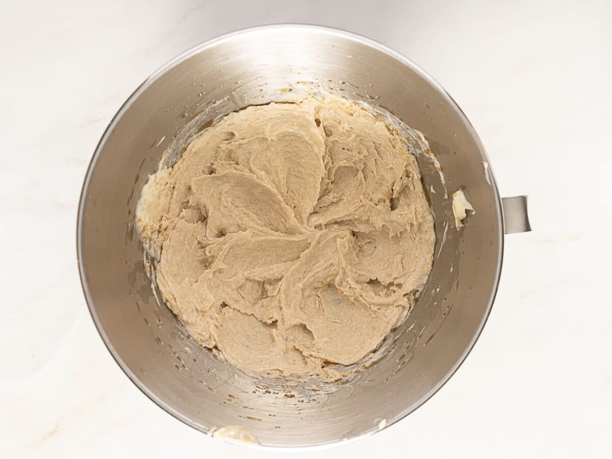 A metal mixing bowl filled with creamed cookie dough sits on a white surface.