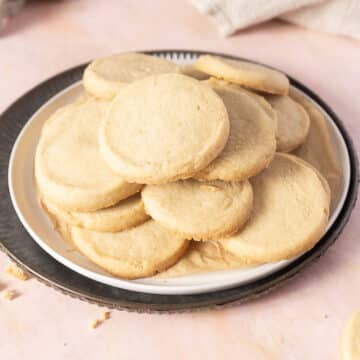 A plate of plain, round shortbread cookies stacked on top of each other, placed on a white and black plate.