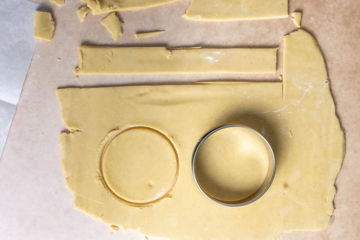 A sheet of rolled-out dough on parchment paper with a round cookie cutter and one circular shape already cut out.