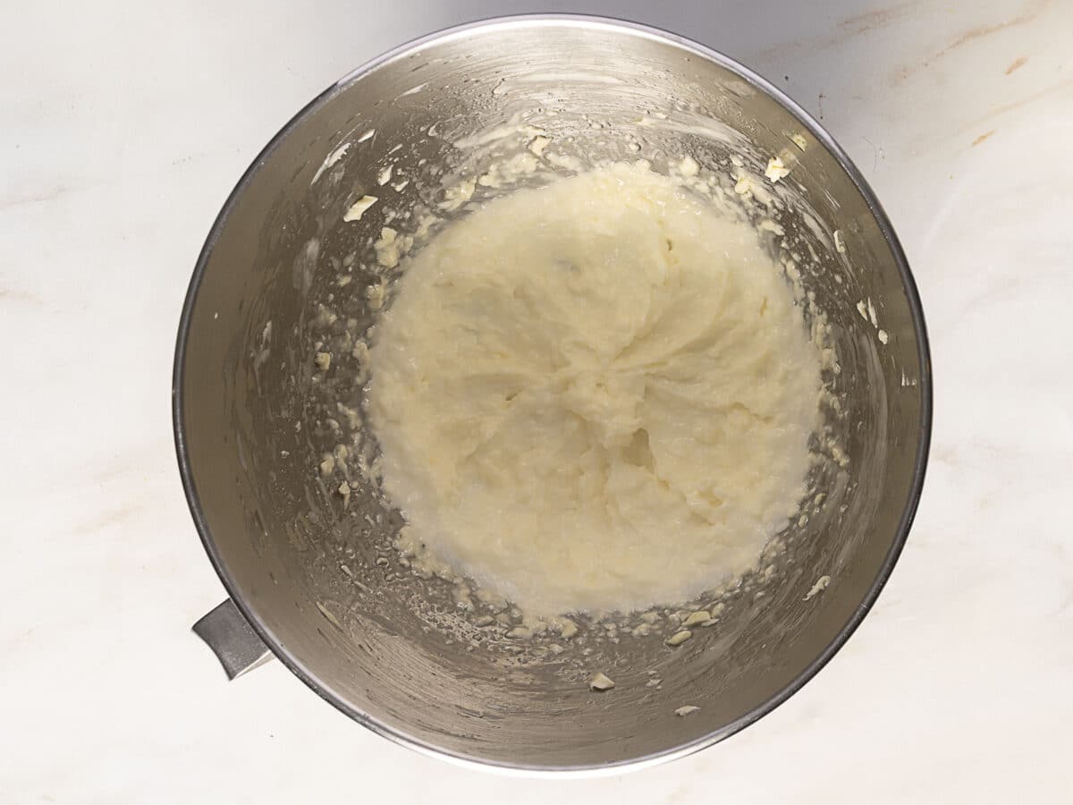A stainless steel mixing bowl containing partially mashed potatoes on a light-colored surface.