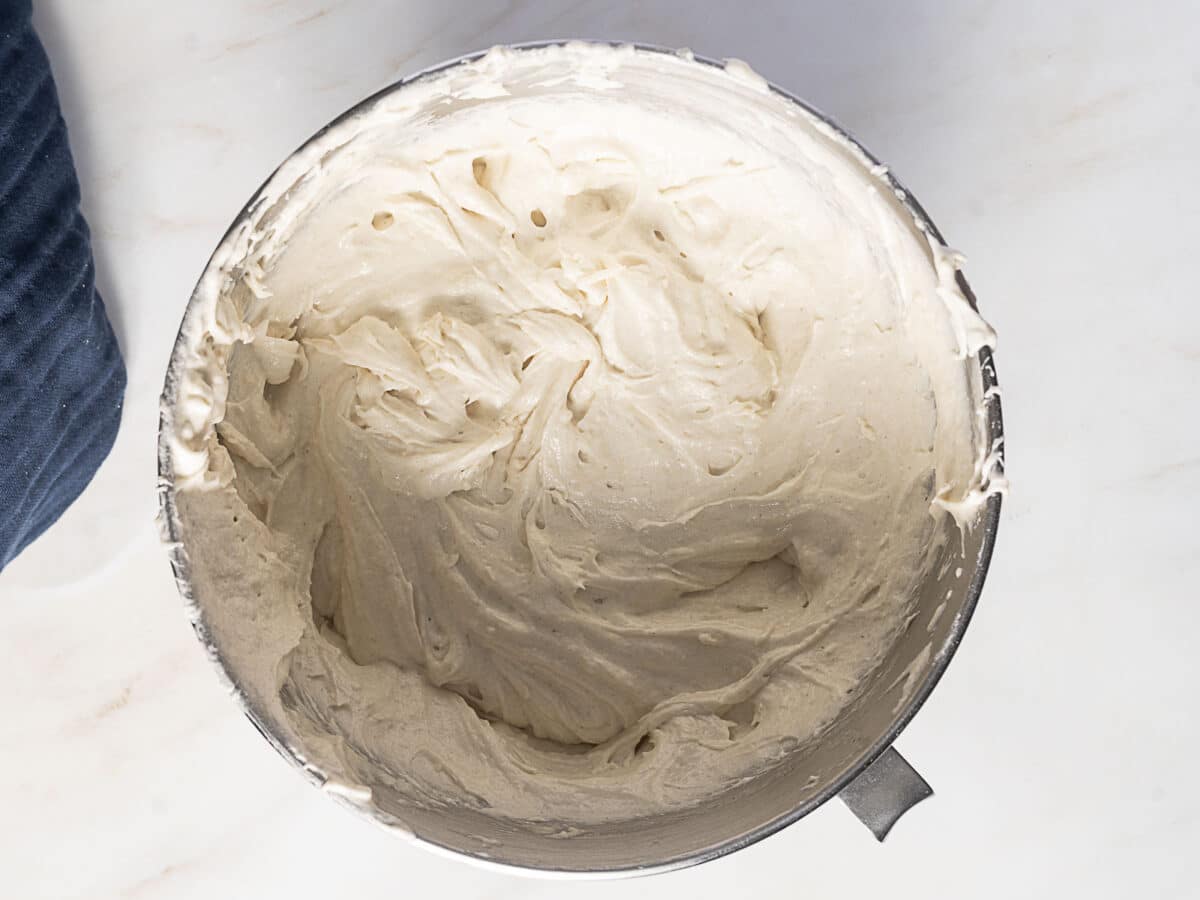 A metal mixing bowl filled with smooth, whipped cake batter on a light-colored countertop.
