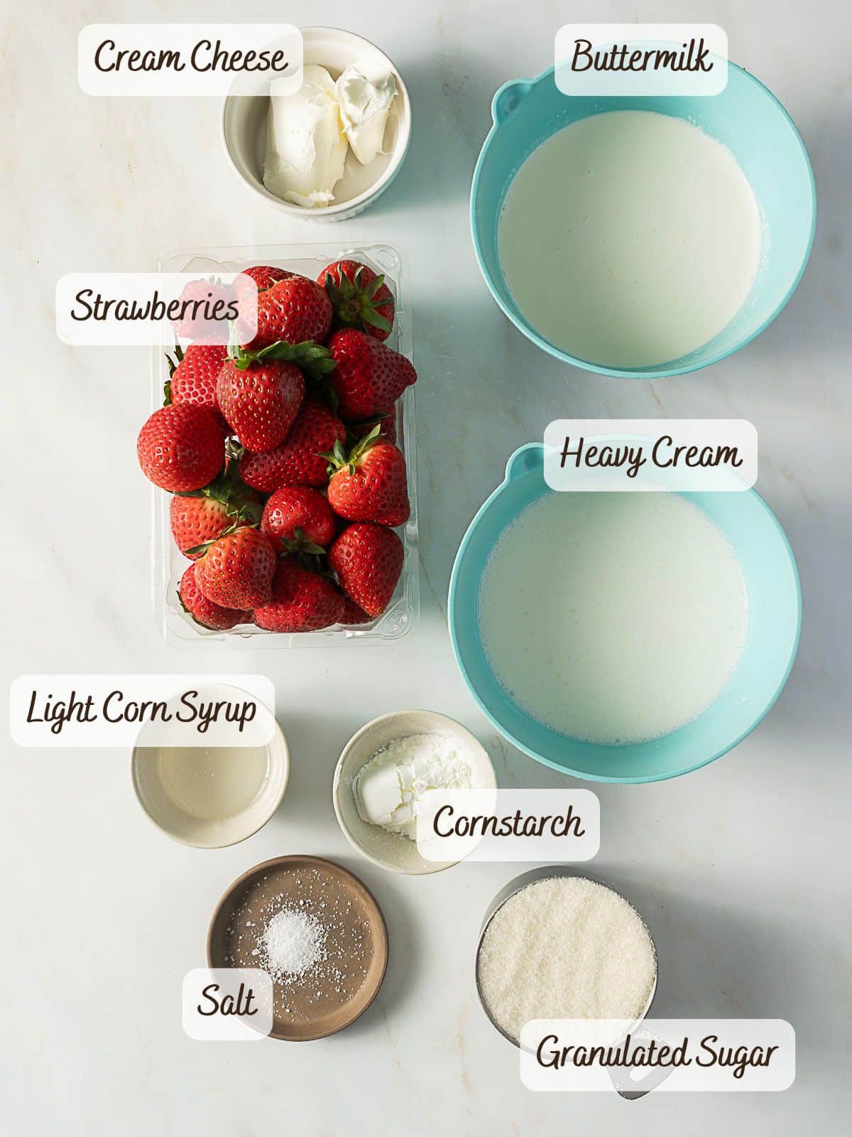Various ingredients are arranged in bowls and labeled: cream cheese, buttermilk, strawberries, heavy cream, light corn syrup, cornstarch, salt, and granulated sugar—perfect for making homemade buttermilk ice cream.