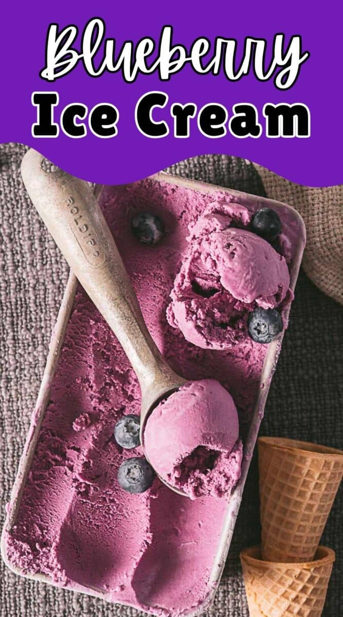 Rectangular container of no eggs blueberry ice cream with a metal scoop, garnished with blueberries, next to two empty waffle cones on a textured surface.