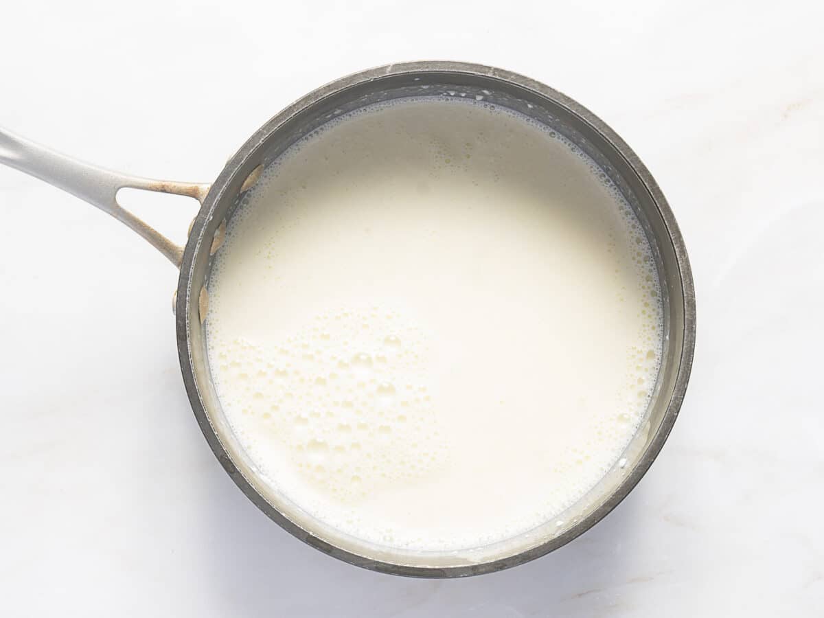 A stainless steel saucepan filled with milk sits on a white marble surface.