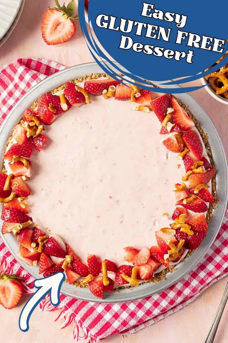 A gluten-free dessert with a creamy pink filling, topped with strawberries and pretzel pieces, arranged on a plate with a checkered red napkin.