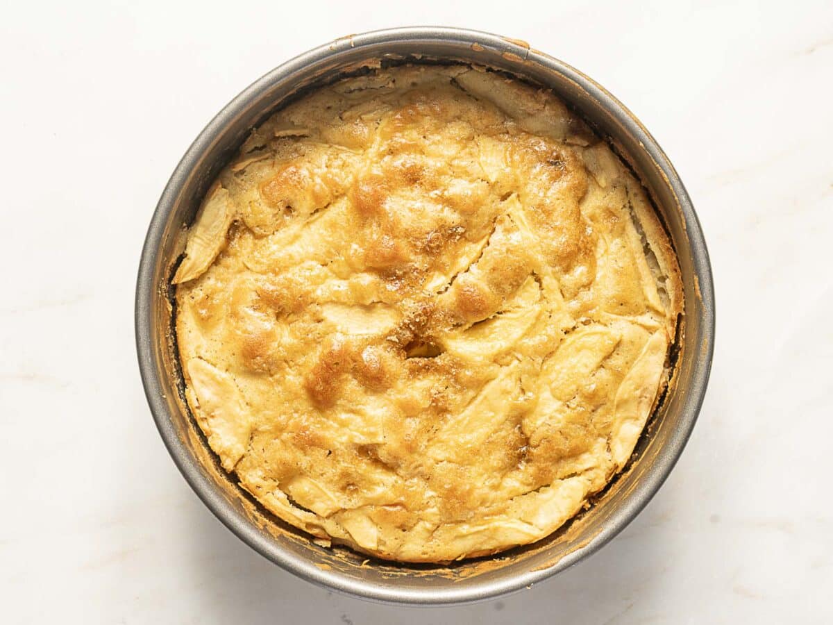 A round, golden-brown baked pie in a metal pan, viewed from above, on a white surface.