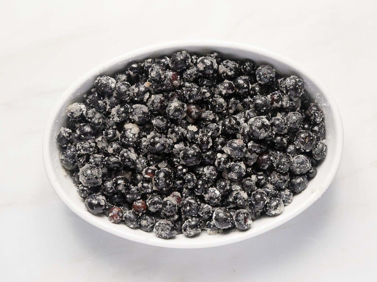 A white oval dish filled with fresh blueberries coated in granulated sugar, set on a white surface.