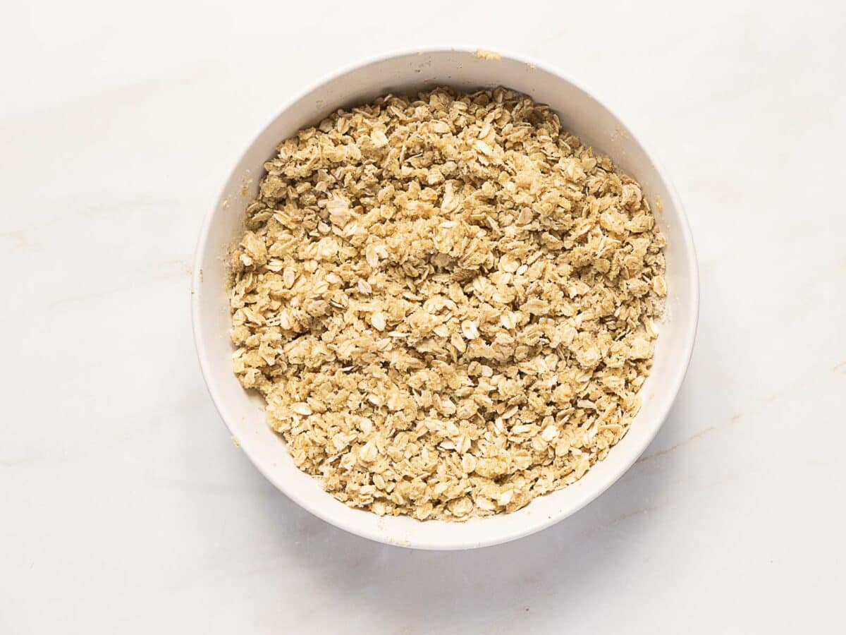 A white bowl filled with dry rolled oats sits on a light-colored surface.