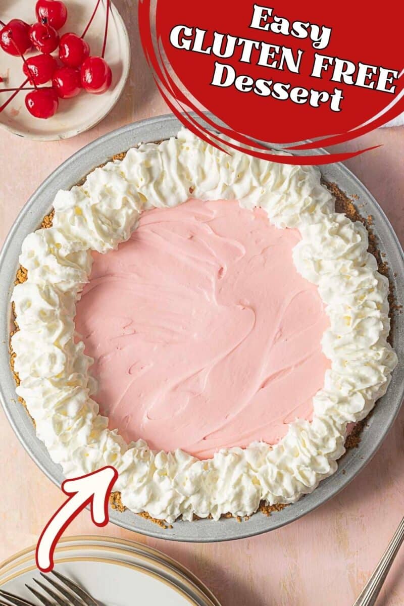 A pie with a pink filling and a whipped cream border sits on a table; a bowl of cherries and forks are nearby. Text reads "Easy Gluten Free Dessert"—the perfect gluten free dessert, no bake required!.