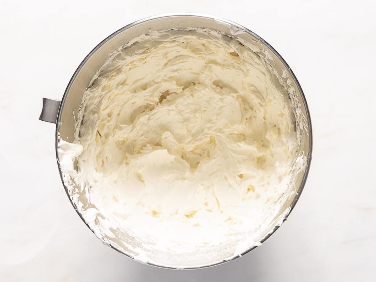 A mixing bowl filled with smooth, whipped cream cheese frosting on a white surface.