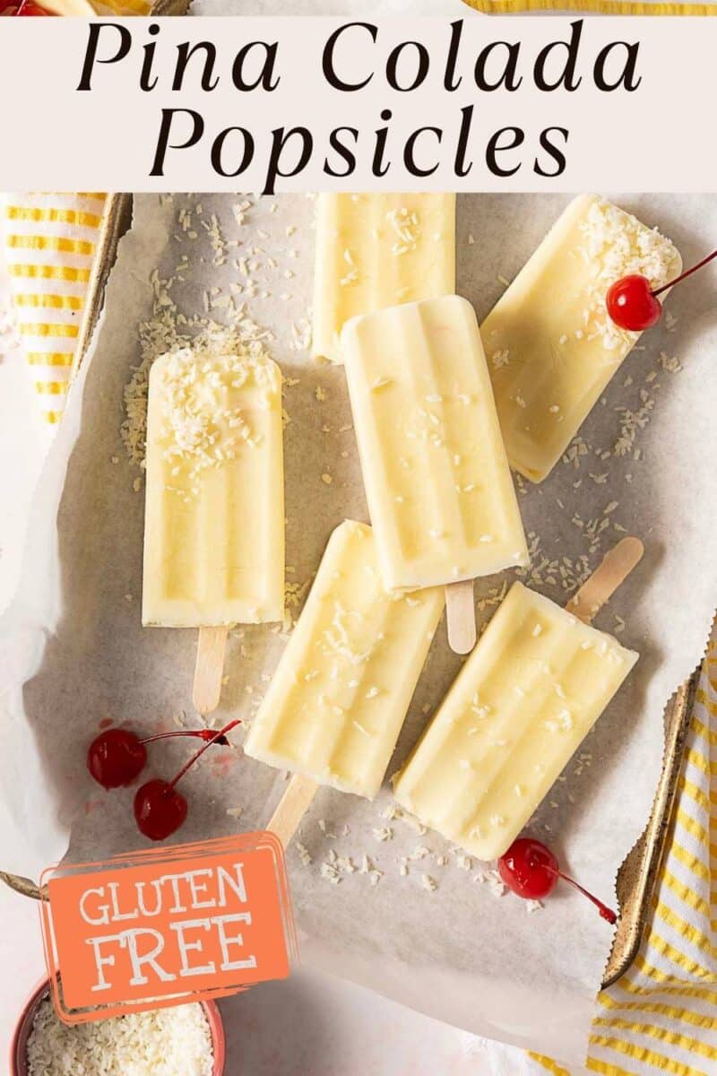 Six creamy yellow pina colada popsicles with shredded coconut and cherries are arranged on a tray.