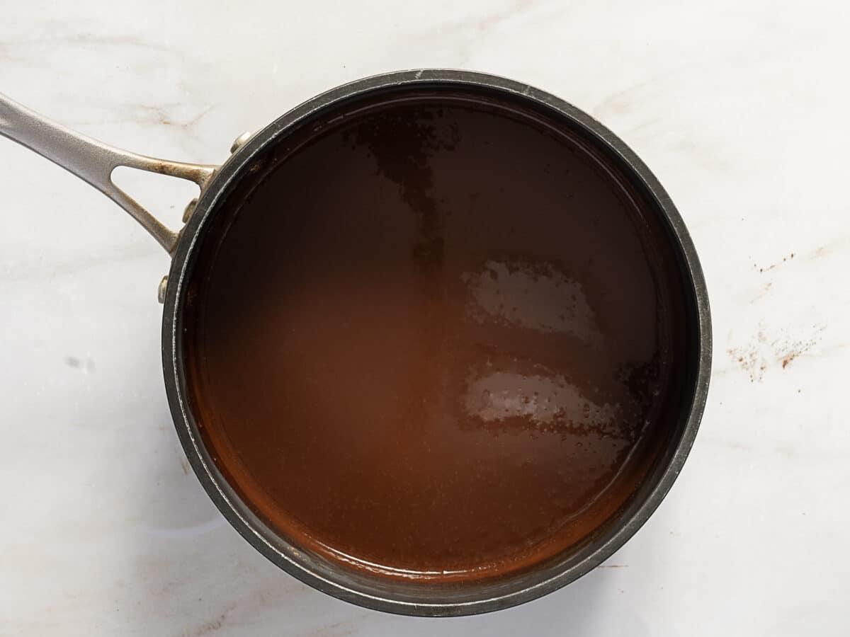 A saucepan filled with smooth, melted chocolate sauce sits on a light marble surface.