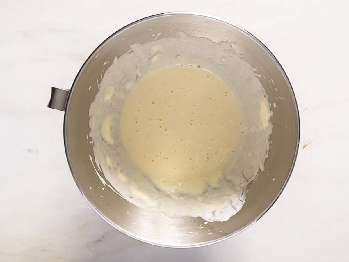 A metal mixing bowl containing a light yellow, slightly frothy liquid batter on a white surface.
