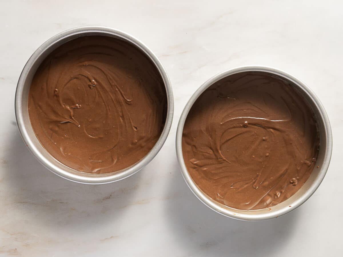 Two round cake pans filled with chocolate cake batter on a light-colored countertop.