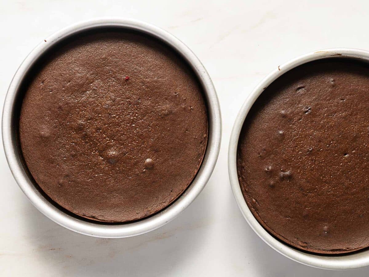 Two round chocolate cakes in metal pans, freshly baked and resting on a light-colored surface.