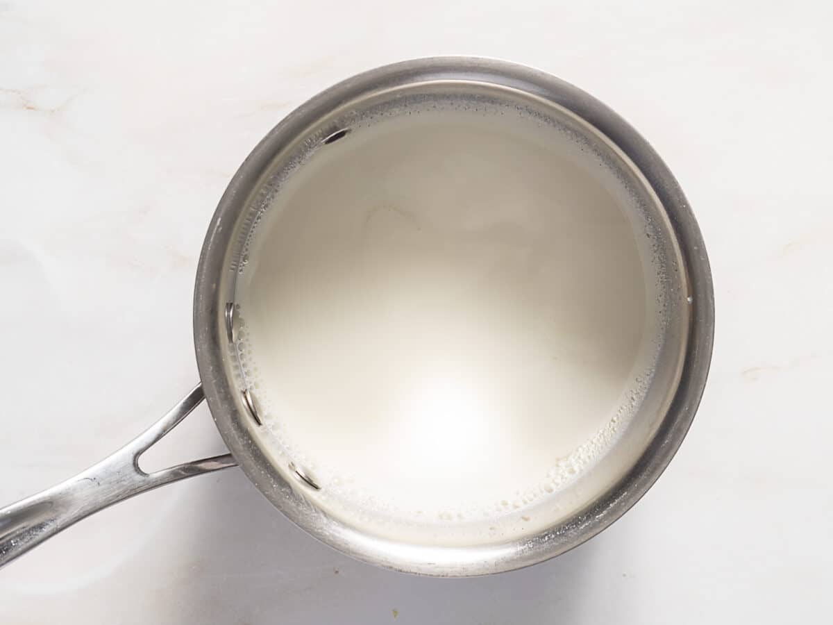 A stainless steel saucepan filled with milk is placed on a white countertop.