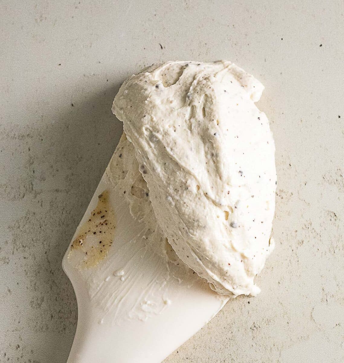 A white spatula holds a mound of creamy, whipped mixture with visible specks on a light surface.