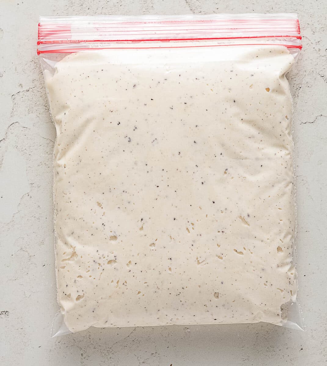 A plastic ziplock bag filled with a creamy, speckled mixture, lying flat on a light-colored surface.