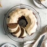 A round bundt cake with light brown frosting sits on a cooling rack, with three slices cut and served on small plates nearby.