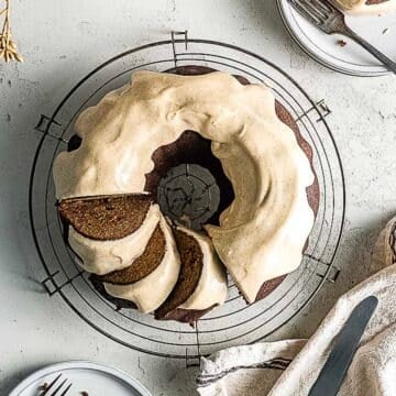 A round bundt cake with light brown frosting sits on a cooling rack, with three slices cut and served on small plates nearby.