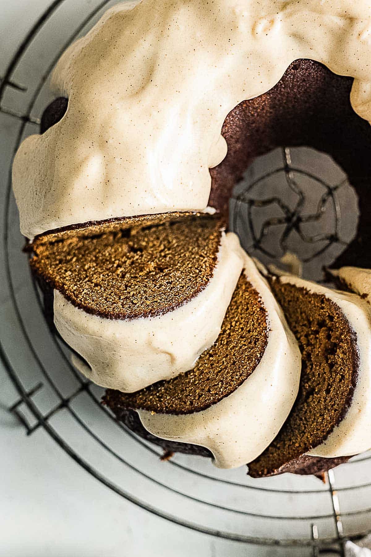 A sliced bundt cake with brown interior and light-colored icing, displayed on a circular wire cooling rack.