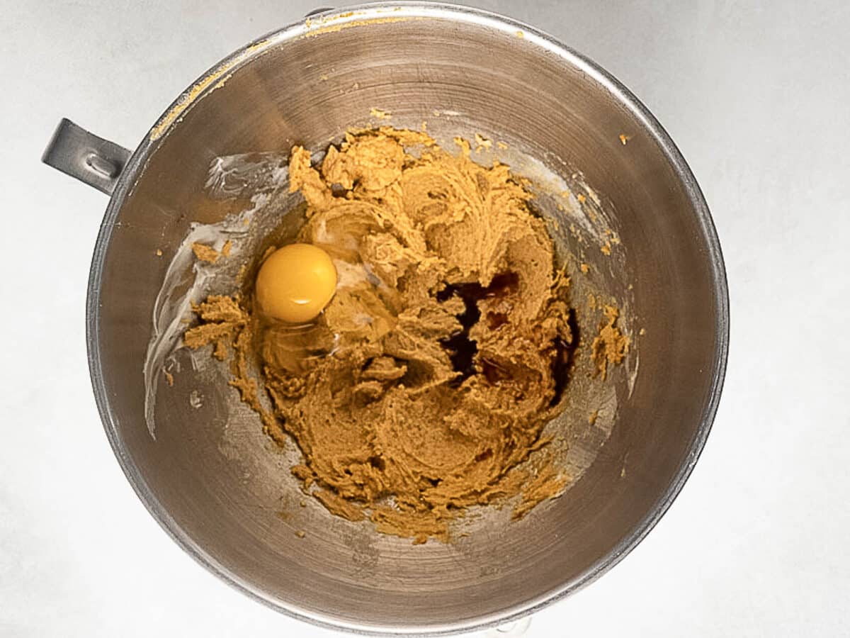 A mixing bowl containing creamed sugar and butter with an egg and vanilla extract added but not yet mixed in.