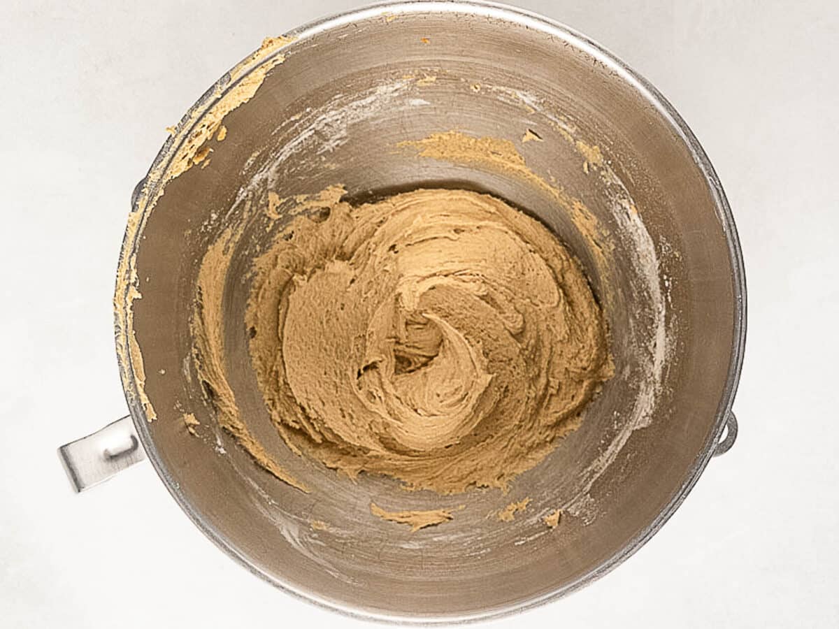 A metal mixing bowl containing a thick, light brown cookie dough mixture partially swirled around the center.