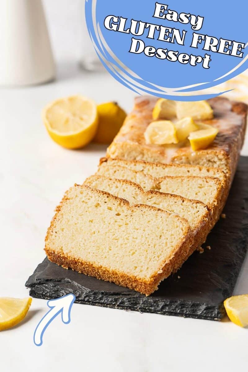 A sliced loaf of gluten free lemon pound cake is displayed on a black slate, adorned with lemon wedges