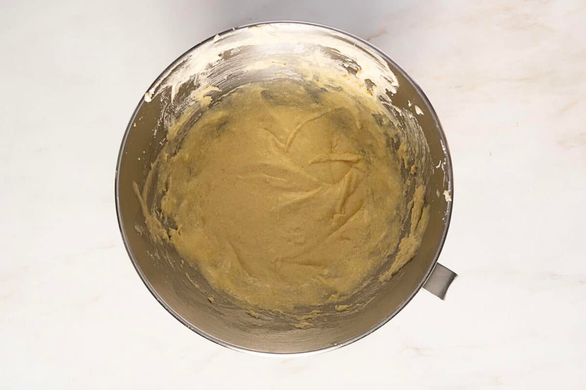 A metal mixing bowl filled with smooth, light-colored dough sits on a white countertop.