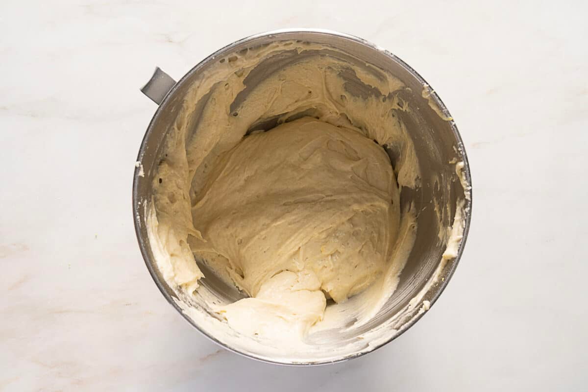 A metal mixing bowl filled with thick, pale batter sits on a white marble surface.